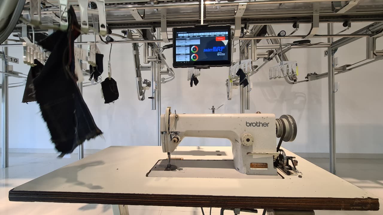 A SmartMRT hanger conveyor station with Octorite's real-time controller tablet mounted above a sewing machine